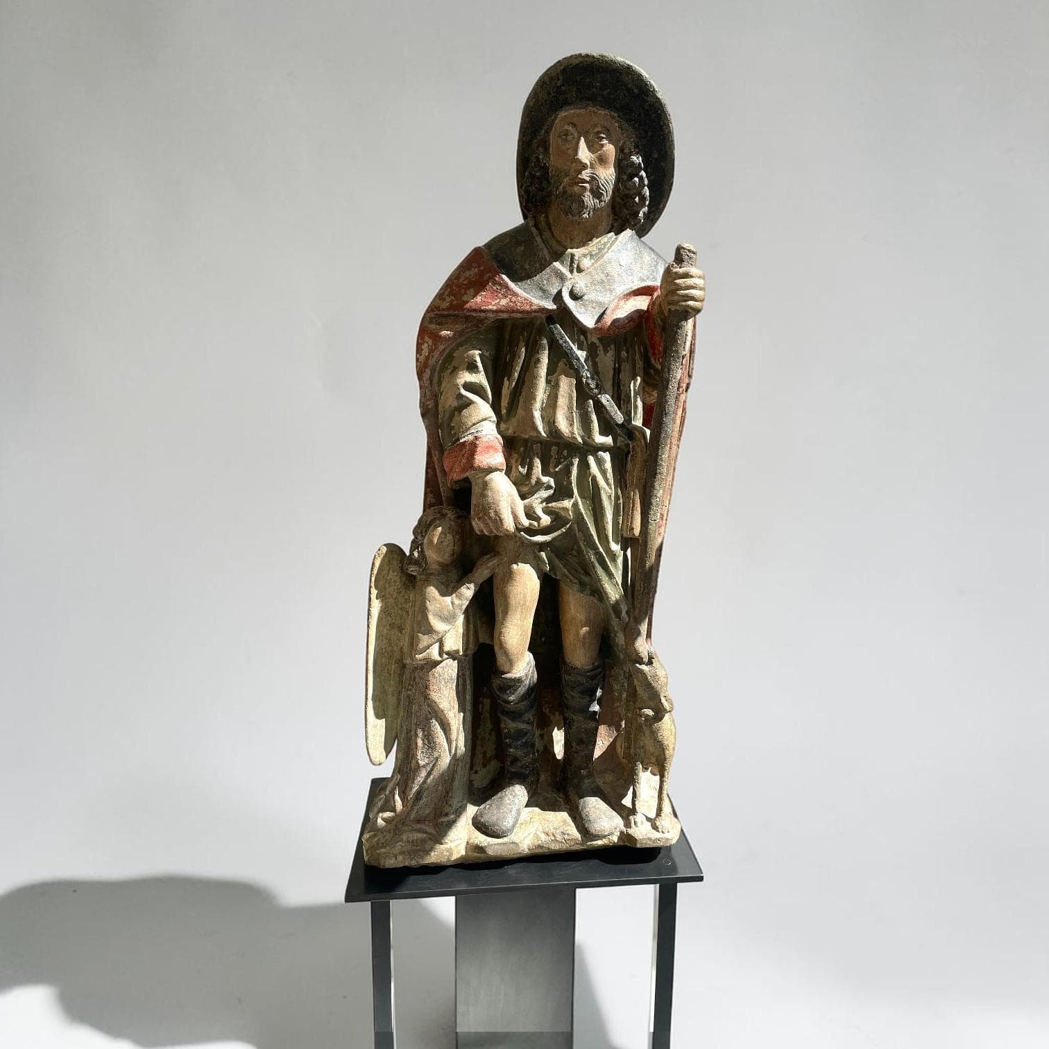 Saint Roch en pierre calcaire sculptée et polychromée, dos ébauché. Coiffé d’un chapeau de pèlerin au bord relevé, le saint tient le bourdon de sa main gauche et soulève, de l’autre, un pan de sa robe pour montrer le bubon sur sa cuisse droite ; à ses côtés l’ange soigneur et le chien ravitailleur.