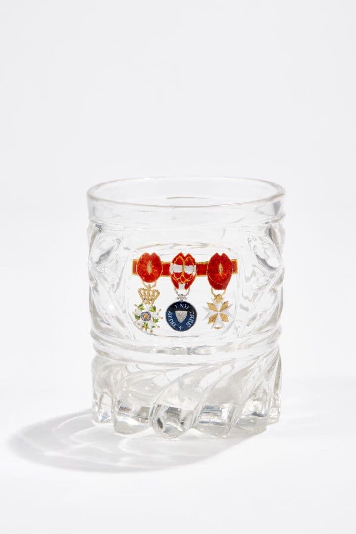 Rare gobelet en cristal moulé taillé en épis, incrusté d'un cristallo-cérame émaillé polychrome sur paillons d'or et d'argent, figurant une croix d'officier de l'Ordre de la Légion d'honneur, une médaille de la Fidélité Helvétique dite «d'Yverdon" (Suisse) et une croix de l'Ordre de l'Éperon d'or (Vatican), sur une barrette. Bon état général, petits éclats à la base.